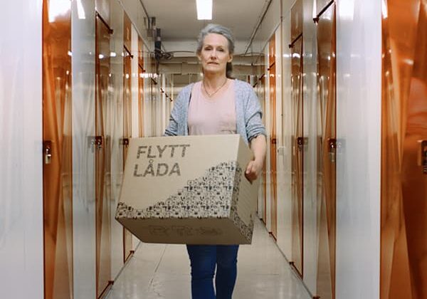 Bild på kvinna gåendes med flyttkartong i en korridor fullt med förrådsutrymmen