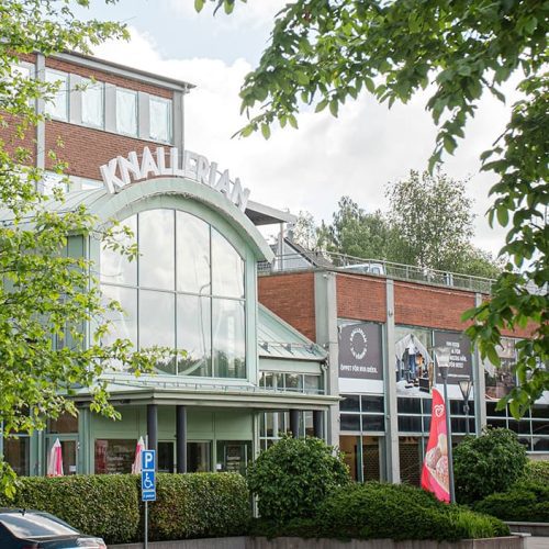 En försommarbild på Knallerians entré. Lummig inramning sett från parkeringen framför ingången.