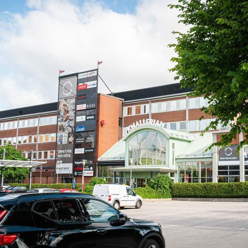 Exteriör bild av fastigheten kallad Knallerian i Borås med entré till galleriagången och parkeringytor framför fastigheten