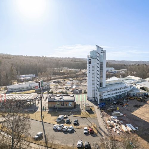 Drönarbild över fastigheten där hotellet tornar upp sig bland mycket parkeringsytor.