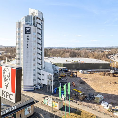 Drönarbild med Jureskogs och KFCs skyltar i förgrunden och hotellets torn syns framför parkeringsyta och i bakgrunden syns E4an.