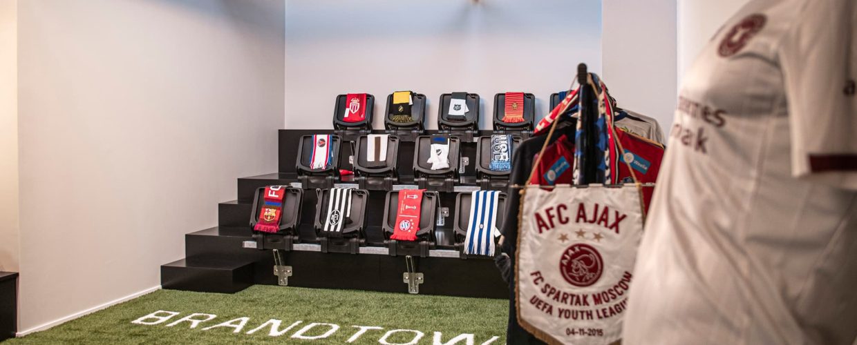 Showroom med gräsmatta och en liten läktare. Halsdukar med olika fotbollslag ligger på läktarplatserna och ställ med kläder från Brandtowns kunder hänger utmed väggarna.