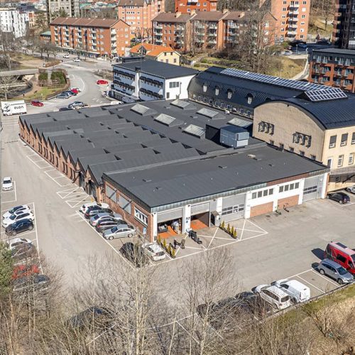 Drönarbild över Forsen sett från baksidan med stora portar för verkstadslokaler. Ån Viskan syns flyta förbi i två väderstreck.